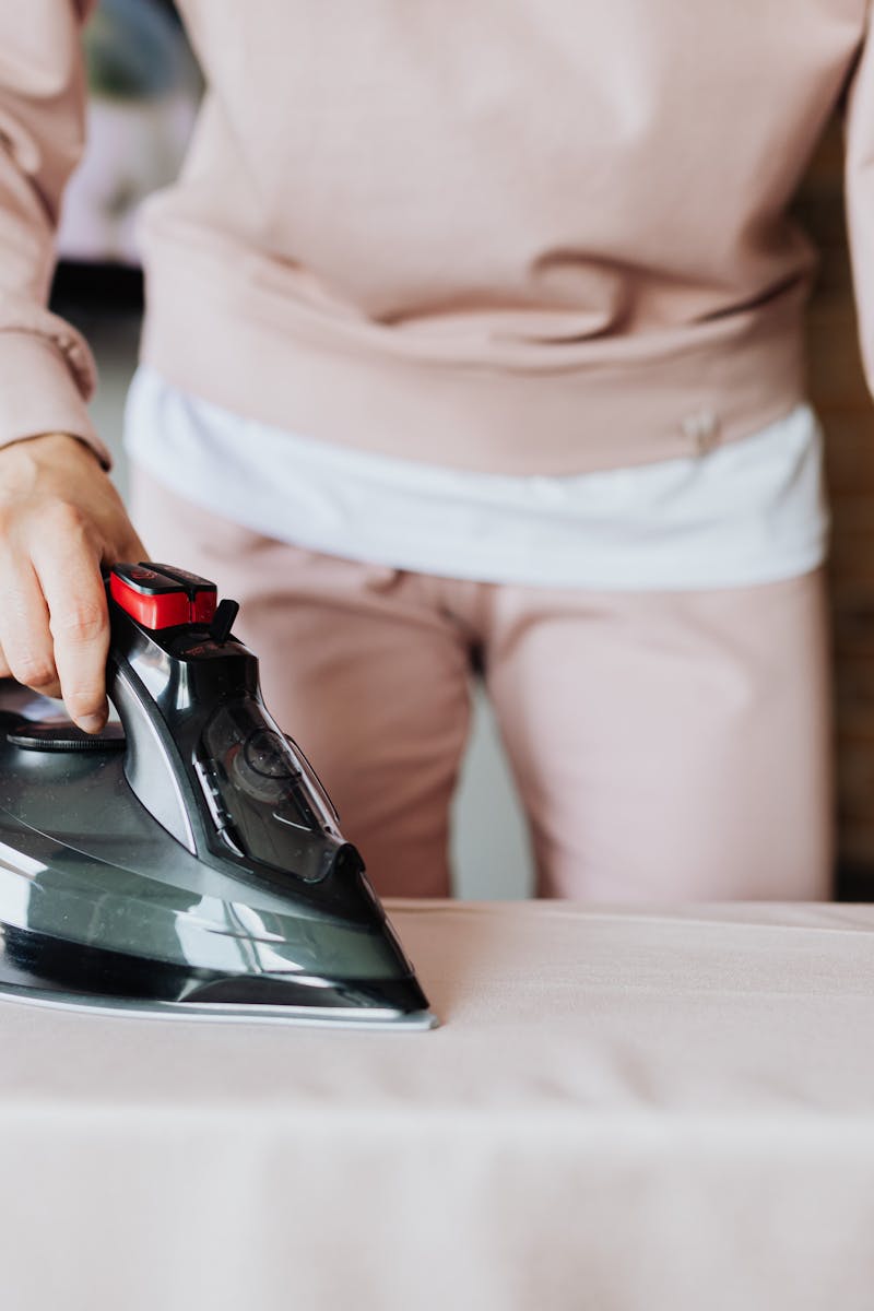 An adult ironing clothes on a board indoors, focusing on housework and fabric care.