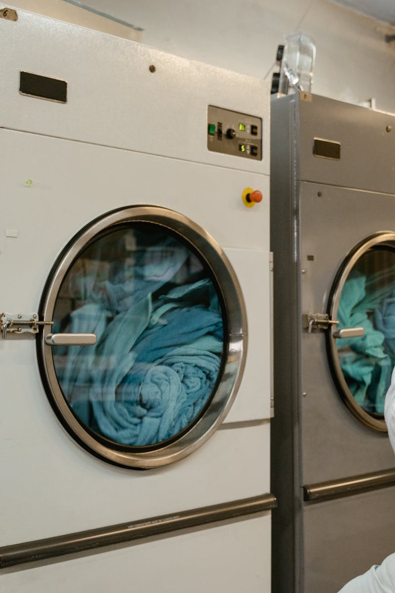 A man wearing a white shirt uses industrial washing machines in a public launderette.